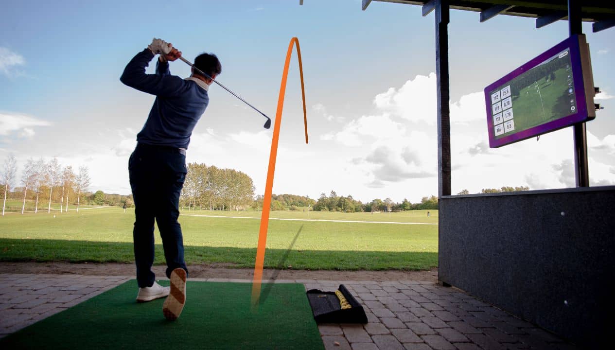 Golfeur en pleine séance de practice simulant un coup de parcours, avec un Trackman installé devant lui.
