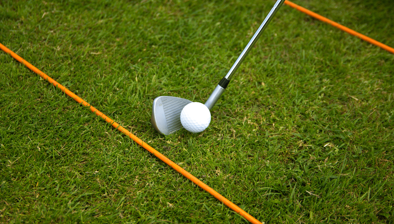 Exercice de golf de la ligne de contact avec deux baguettes d’alignement posées parallèles au sol et une balle placée entre elles.