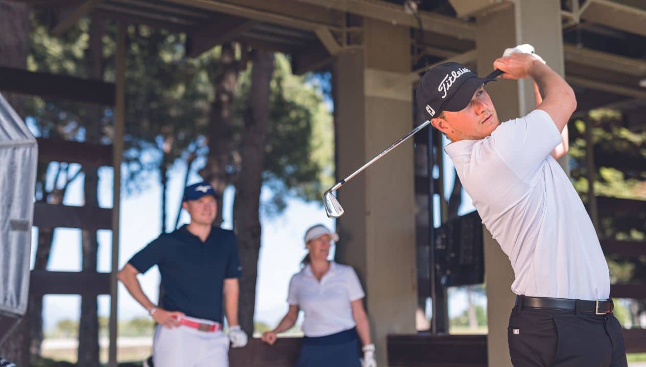Trois golfeurs s’entraînant côte à côte au practice, chacun concentré sur son swing.
