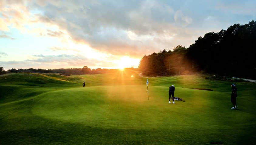 jouer au golf en automne Golfeur sur un green au coucher du soleil en automne, lumière dorée sur le parcours.